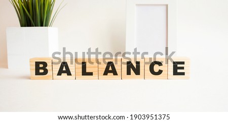 Wooden cubes with letters on a white table. The word is BALANCE. White background with photo frame, house plant.