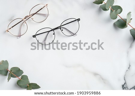 Woman's eyeglasses and eucalyptus branches on marble background. Flat lay, top view. Royalty-Free Stock Photo #1903959886