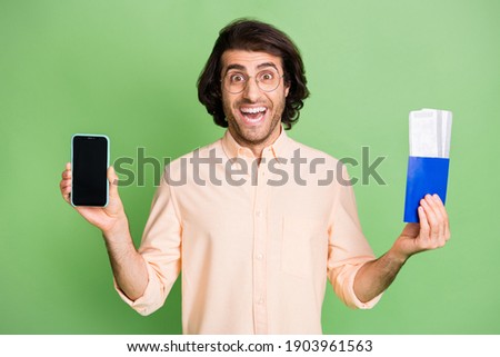 Portrait of attractive cheerful guy holding in hands gadget air ticket use app booking check-in isolated on bright green color background