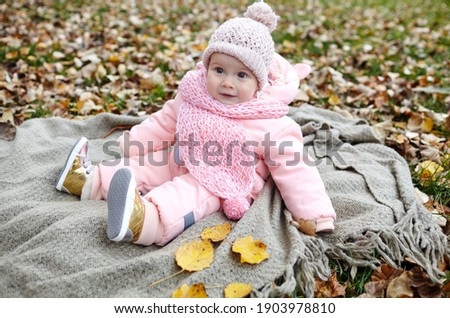 Beautiful baby girl sitting on the plaid. Child outdoor. Adorable little girl in warm clothes at picnic in autumn park on sunny day. Pretty little girl