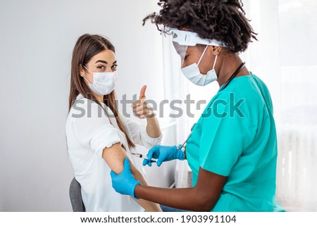Girl Gesturing Thumbs-Up Receiving Coronavirus Vaccine Injection In Hospital. Covid-19 Vaccination.  Corona Virus Protection, Cure And Medication. Woman getting a COVID-19 vaccine