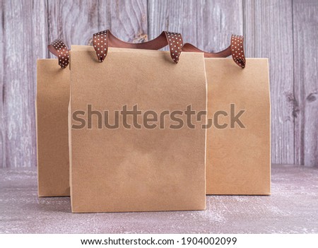 Brown paper bag packaging with ribbon handles placed on a gray stone background with a wooden wall. Side view with copy space for text.
