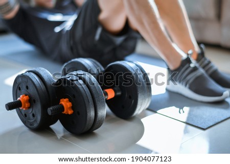 Exercises at Home. Active Asia man in T-shirt and Shorts doing Crunch in living room. dumbbells on pictures lying on floor.