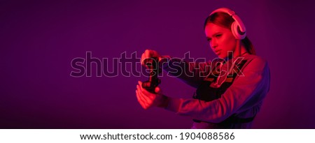 KYIV, UKRAINE - NOVEMBER 27, 2020: young woman in headphones playing video game on purple background, banner