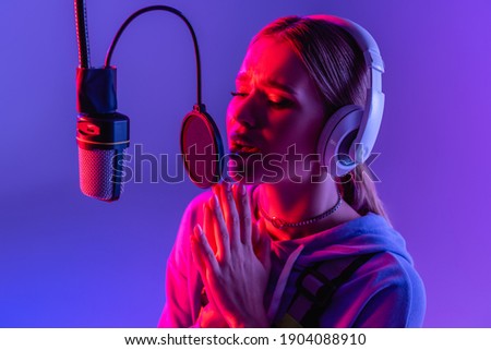 young woman in wireless headphones recording song while singing on purple with color filter