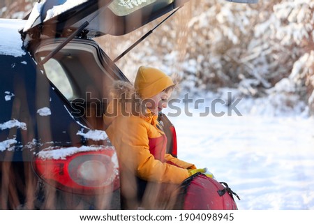Adorable boy with hot tea or cocoa in his hands sitting in black car at winter day. Road trip,getaway, natural environment, staycation, travel, tourism at winter time.