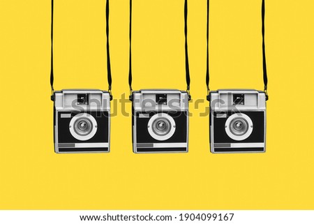 some gray and black retro film cameras, hanging from their strips, on a yellow background