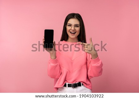 Photo of attractive lady in glasses hold telephone read, write posts on blog. Wears casual pink t-shirt white pants isolated pink color background.