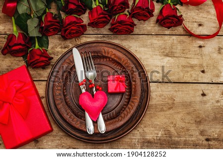 Romantic dinner table. Love concept for Valentine's or mother's day, wedding cutlery. Bouquet of fresh burgundy roses, vintage wooden boards background, rustic style, top view