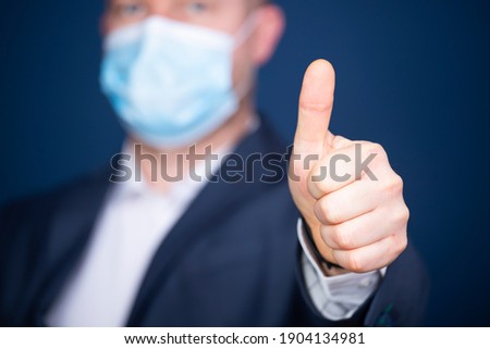 Businessman with medical mask showing OK sign or thumb up. Excellence of the business or service concept.