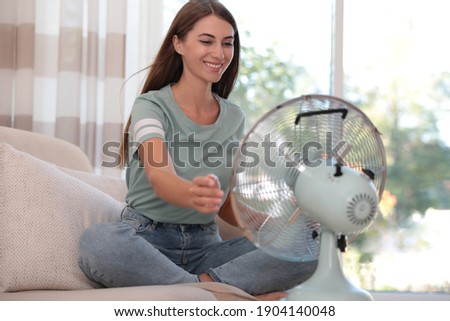 Woman enjoying air flow from fan on sofa in living room. Summer heat Royalty-Free Stock Photo #1904140048