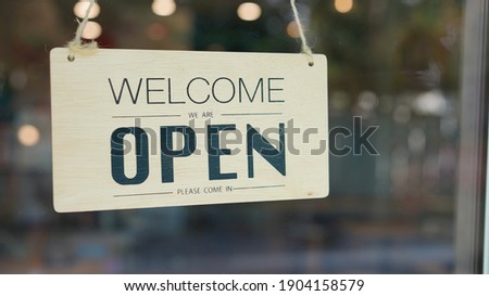 Open and closed flip sign in front of coffee shop and restaurant glass door. Wooden sign with wording of place's status. Say Welcome. We're OPEN. Please come in.