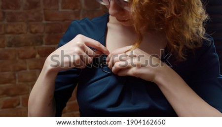 Close up of young woman attaching lavalier microphone to dress preparing for interview. Female journalist or reporter clipping microphone on clothes preparing for tv show