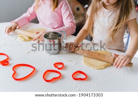 Little girls, sisters cooking homemade heart shaped cookies for valentine's day. Holiday for all lovers. Gift, surprize for mom. Red molds, rolling pin, flour, dough.Handmade family, bakery with kids.