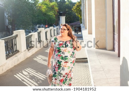 Beautiful woman dressed in summer dress  and glsses walking outdoor in the street of the city . Style overweight girl outdoor.