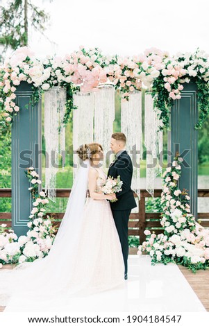 Beautiful caucasian Wedding couple is standing in front of decorated with pink roses archway and holding hands, wedding ceremony, wedding vows