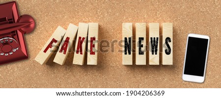 wooden blocks as domino blocks with the message FAKE NEWS surrounded by a smartphone and a vintage phone on cork background