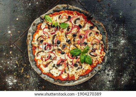 A top view of appetizing Vegetarian pizza with black dough and various vegetables