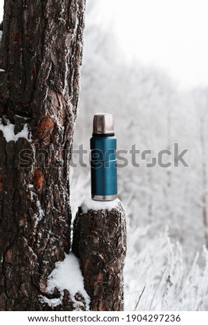 Camping vacuum flask and winter wood. Thermos standing on a stump. Hot drink in cold weather concept. Vertical photo