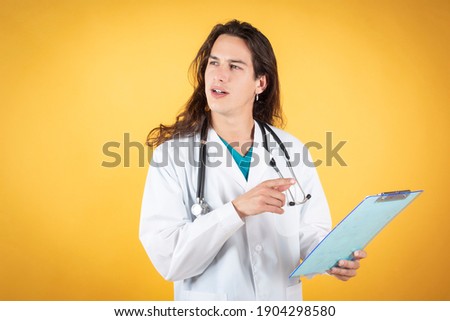 long haired male doctor with folder and stethoscope, yellow background, copy space