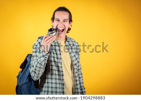 handsome and smiling blue-eyed man, wearing casual clothes,with a backpack he bites his camera,yellow background copy space
