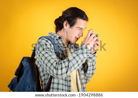Happy serious handsome young man, caucasian, with a camera and backpack, digital nomad, traveler, yellow background, copy space.