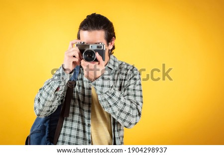 Handsome young man, caucasian, with a camera and backpack, digital nomad, yellow background, copy space.