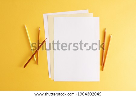 Colorful pencils and empty white papers . Empty place for text or drawing on the yellow background.
