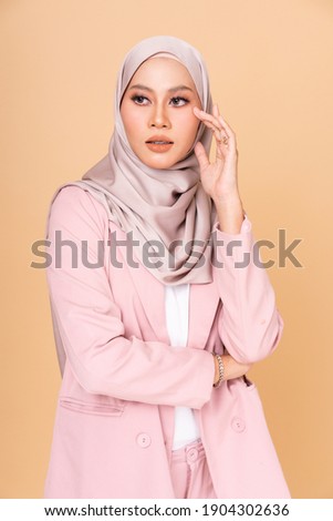 Portrait of a beautiful Muslim female model wearing stylish pink office attire with hijab isolated over beige  studio background. Fashion, beauty, style concept.