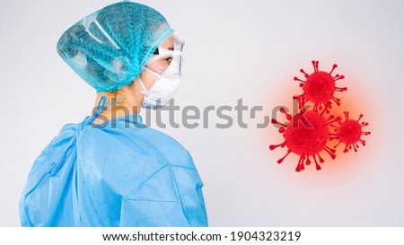 Rear photo of a doctor with protective equipment and goggles looking at an enlarged picture of red covid 19 virus. Virus spread concept on white background.