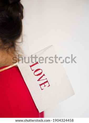 Woman in red sweater holding a checkbox with the word love on a white background. Close-up. Daylight, indoor. Happy Valentine's, Happy Mother's Day, World Women's Day, holiday and festive concept.