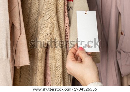 Woman customer looking on tag choosing sweater with christmas ornament in garment store. Shopping. Winter 