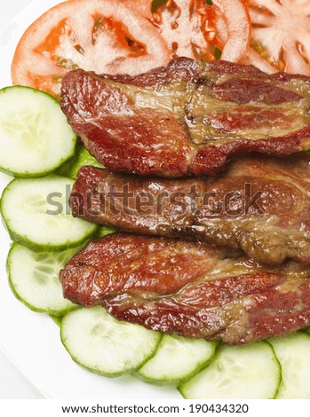 Beautifully grilled and slightly smoked pork cuts served o white plate with cucumbers, tomato and fries