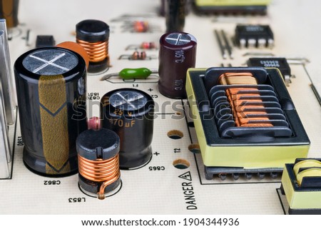 Electronic components on printed circuit board detail. Close-up of capacitors, inductors and rectangular transformer with protruding insulation grooves in copper wire winding. Electrical engineering. Royalty-Free Stock Photo #1904344936