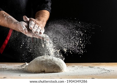 Beautiful and strong men's hands knead the dough make bread, pasta or pizza. Powdery flour flying into air. chef hands with flour in a freeze motion of a cloud of flour midair.