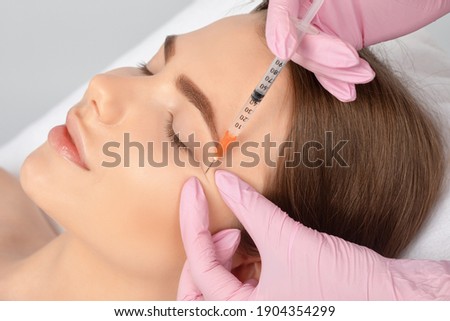 Cosmetologist makes rejuvenating anti wrinkle injections on the face of a beautiful woman. Female aesthetic cosmetology in a beauty salon. Royalty-Free Stock Photo #1904354299