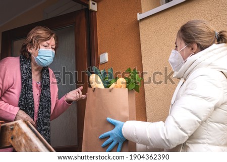 Helping hand with shopping food during pandemic outbreak. Volunteer wearing ffp2 mask during delivering groceries to senior woman. Support local elderly community due covid-19 lockdown Royalty-Free Stock Photo #1904362390