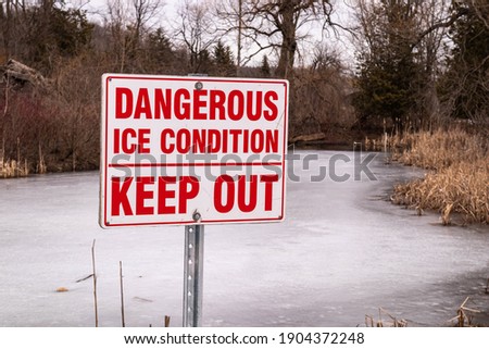 A closeup of the "Dangerous Ice Condition" signage in the snowy pond during the winter season