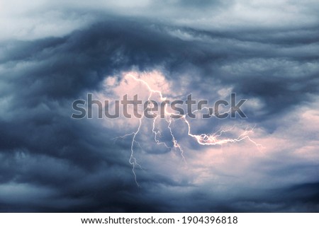 A terrible dangerous storm with a strong wind swirls thunderclouds in the mountains with fabulous twists, from which rain and hail or a thunderstorm with lightning flies. Royalty-Free Stock Photo #1904396818