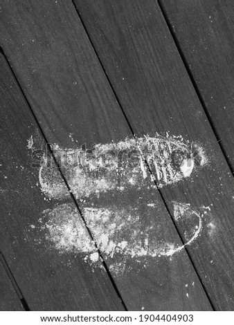 Top down view of two sandy shoe prints on a boardwalk, in black and white