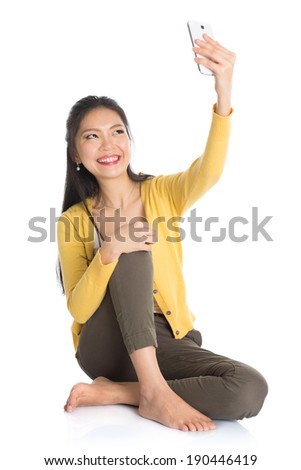 Full body Asian girl selfie or self photographing, sitting on floor, isolated white background.