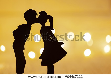 in the foreground is a silhouette of a guy and a girl, they kiss, in the background is not in the focus of the garland