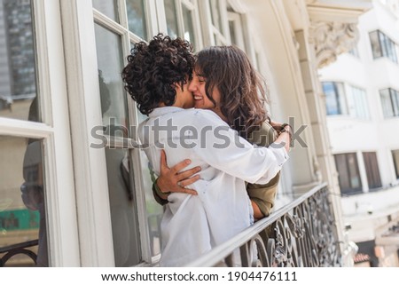 Stock photo of happy couple standing in their balcony smiling and hugging.