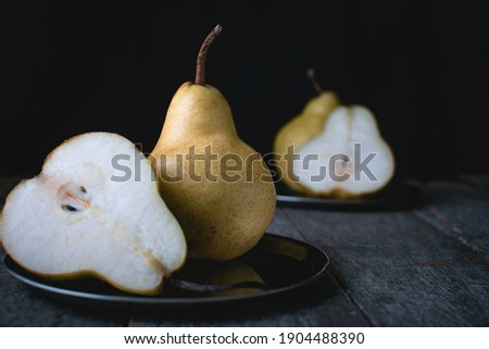 Horizontal photograph of pears on a metal tray and rustic wood with a black background. Dark moody style