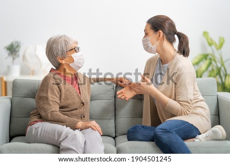 Beautiful mother and daughter are talking and smiling while sitting on couch at home.