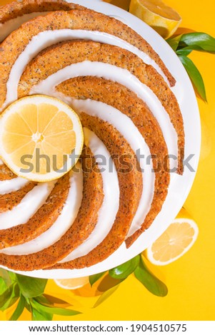 homemade lemon poppy seed bundt cake with fresh lemon slices isolated on bright yellow background