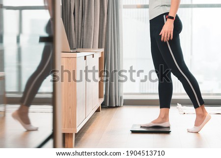 A healthy woman standing on a scale to measuring her weight in the living room after home workout in the morning. Body mass index - BMI, Hormones, Weight Loss, ideal healthy weight, Metabolism, Diet. Royalty-Free Stock Photo #1904513710