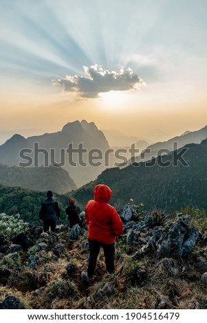 Adventurers wearing a red hoodie with mountains and dusk near the sunset in the background of Doi Luang, Chiang Dao, Chiang Mai, Thailand. Taking a photo from the summit.