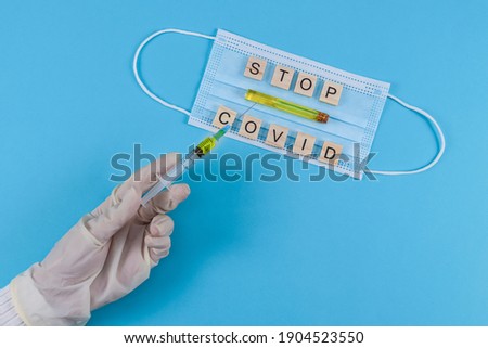 Syringe in hand and mask with vaccine with the inscription stop covid on a blue background, top view close-up.