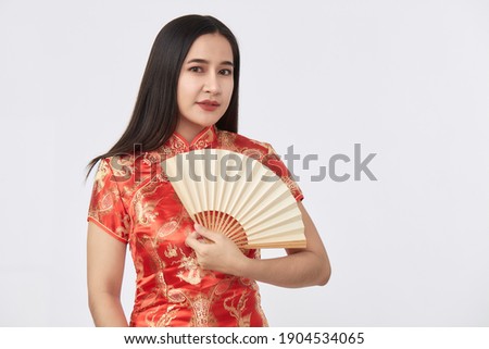 Attractive beautiful Young Asian woman in traditional red cheongsam dress holding Chinese fan for Chinese new year in light gray isolated studio background